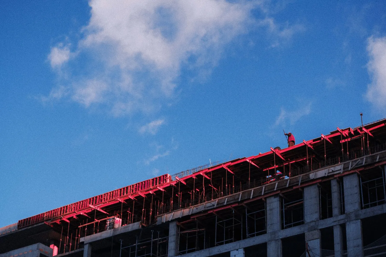 A building under construction with scaffolding against a bright blue sky, captured from a low angle.